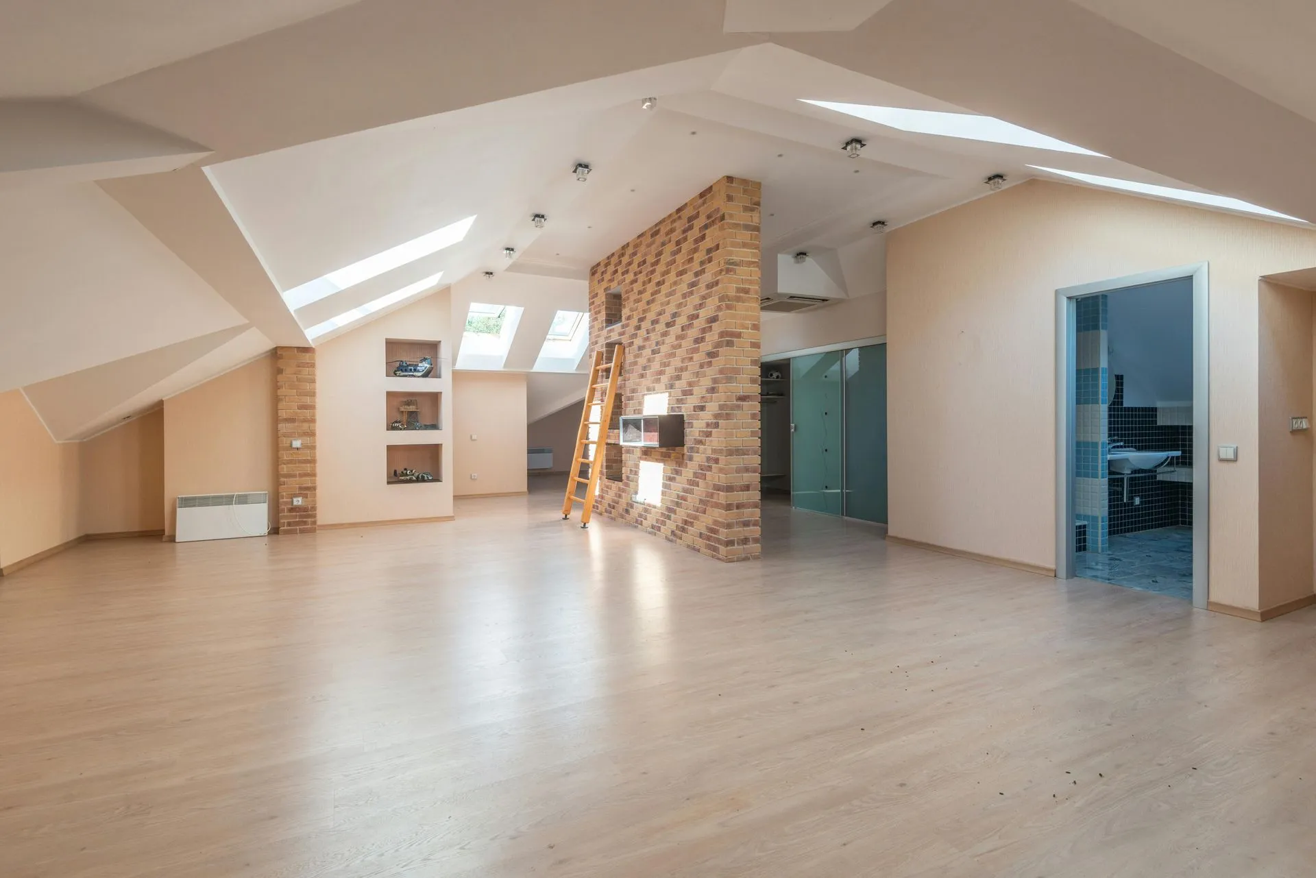 An empty attic with hardwood floors and a brick wall.